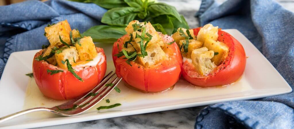 Three Egg-Stuffed Baked Tomatoes with Garlic Croutons on a white plate