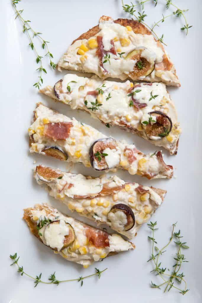 Fig Prosciutto Pizza with Cauliflower Ricotta Truffle Puree cut up on white plate with herbs