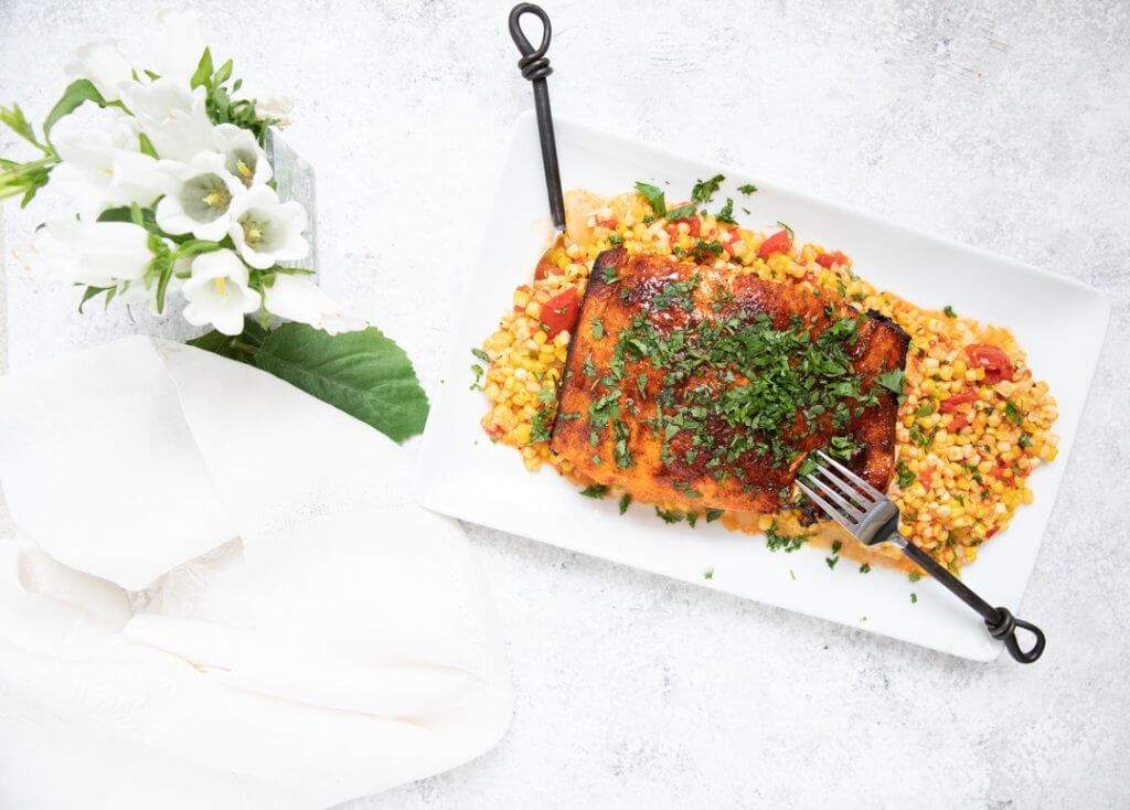Grilled Glazed Salmon with Tomato Corn Saute on marble countertop with flowers