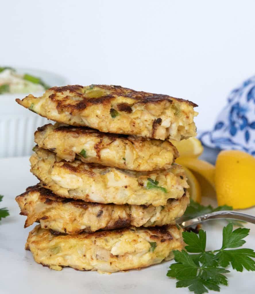 Chicken cakes stacked up in a pile with a bowl of cole slaw in the background