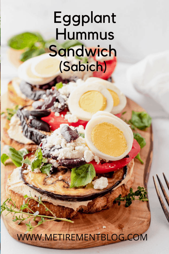 Vegetable sandwich of sliced tomatoes and roasted eggplant, hummus, kalamata olives, goat cheese and hard boiled eggs on a sourdough bread on a wooden board 